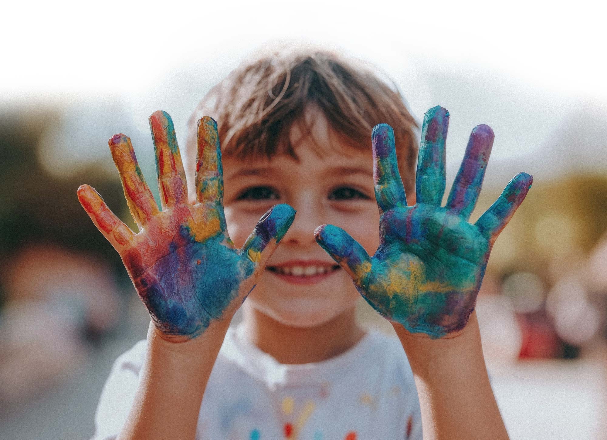 Kind zeigt bunte Farbhände. Symbol für Vielfalt und spielerische Entwicklung.