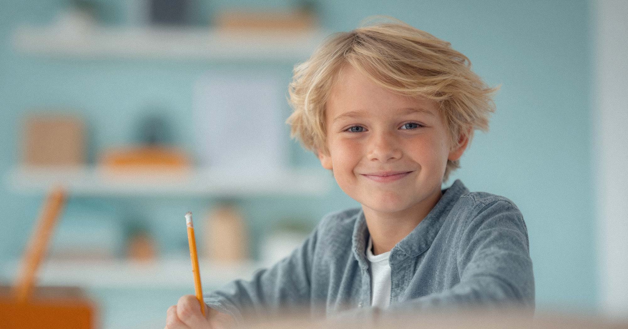 Junge sitzt lächelnd am Schreibtisch mit Stift. Individuelle Kinderbetreuung stärkt Vereinbarkeit im Familienalltag.